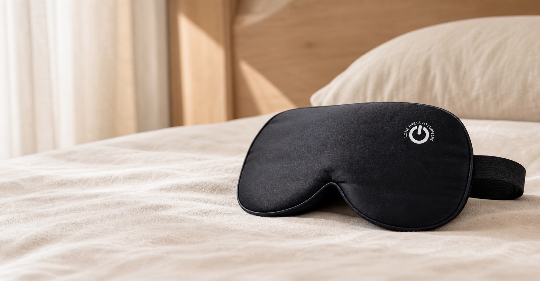 COOVOAMAE black silk heated eye mask resting on warm cream linen in a calm bedroom